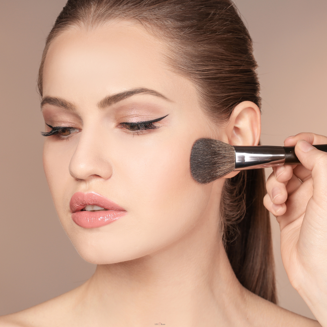 Woman applying makeup with a brush on a neutral background
