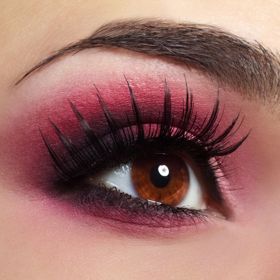 Close-up of a eye with dramatic makeup featuring pink and purple shades and long false lashes.