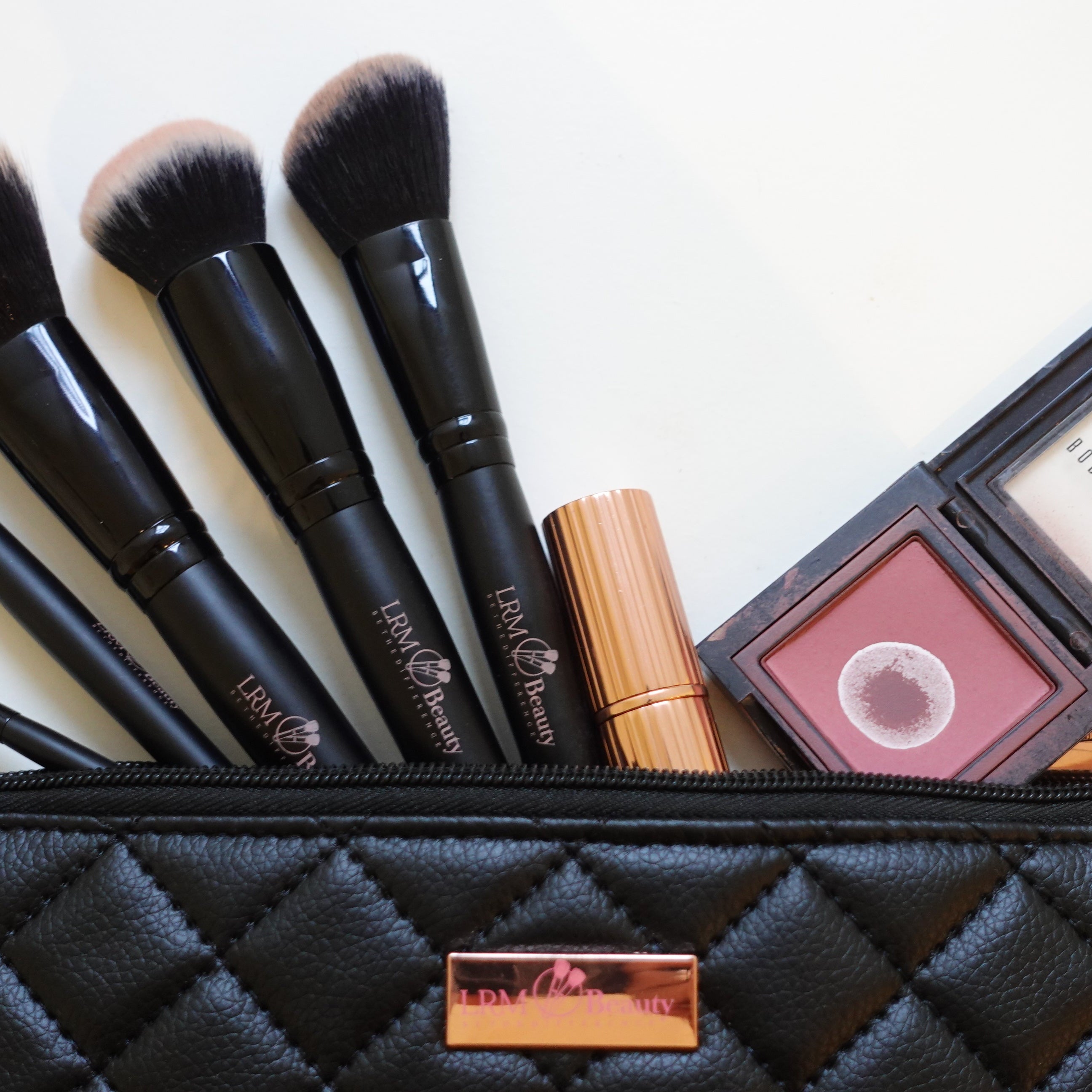 Makeup brushes and products in a black quilted pouch on a white background